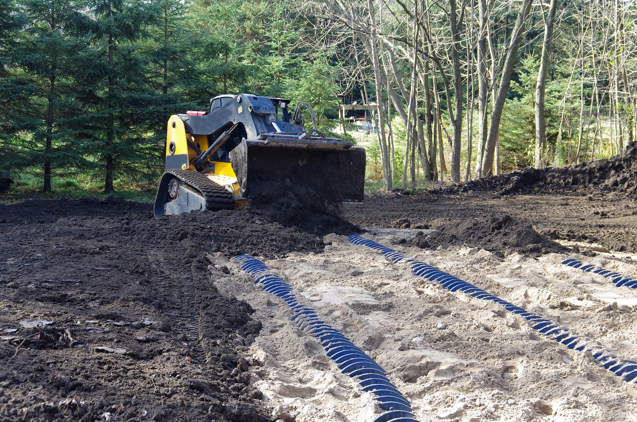 Skid steer installing drainage pipes for a septic leach field in Illinois